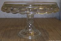 Side angle showing clear glass cake stand with scalloped edging and patterned pedestal base.