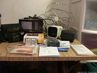 Full view of lot items including Kodak camera with case, Samsung camera in box, Polaroid case, manuals, and other accessories on wooden surface