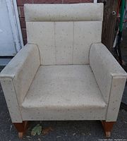 Front view of child rocking chair showing cream upholstery with speckles, wooden rocker base, padded armrests, and backrest.
