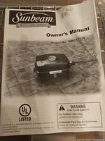 Photo of the owner's manual for the Sunbeam Electric Grill model NBC1712E with warning and UL listing visible.
