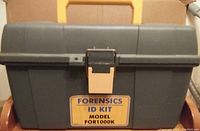 Closed gray plastic toolbox with yellow handle and latch labeled 'Forensics ID Kit Model FOR1000K'