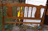 Front view of full size wooden headboard resting outdoors showing design and condition