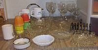Overview of lot items on wooden surface including glass bowls, mugs, colorful plastic cups, glass drinking glasses, and metal toast rack.
