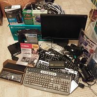 Top view photo showing multiple keyboards, a monitor, various cables, a Canon value pack, a box for Cyber Modem, and assorted electronics scattered on a floor surface.
