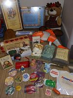 Photo showing a variety of decorative figurines, plush toys, plaques, and pin buttons arranged on a table.