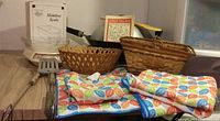 Overall view of kitchen items including the scale in box, woven baskets, colorful oven mitts and pot holders, and spatula