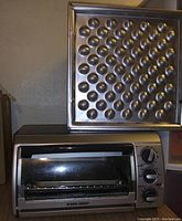 Photo showing stainless steel Black & Decker toaster oven with glass door closed, placed under metal muffin pan with 24 cups.
