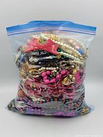 Plastic bag packed full of mixed colorful crafting jewelry including beads, bracelets, chains, and decorations