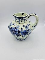 Side angled view of vintage Blue Delft pitcher showing body shape and floral pattern in blue on cream base.