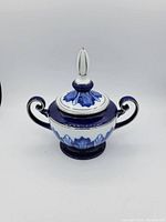 Front view of vintage Bombay lidded dish showing floral design, lid with finial, double handles, and pedestal base.