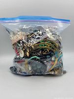 Clear plastic zipper bag containing a dense mix of jewelry pieces, showing various colors and metal components inside.
