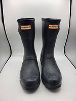 Front view of a pair of black Hunter rain boots with visible red and white Hunter logo on front.