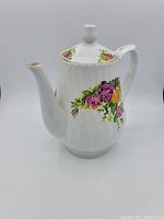 White porcelain coffee pot with ribbed texture and floral pattern on front and back, gold trim on spout and lid edge, round finial lid handle.