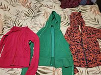 Three Lululemon hoodies laid out on bed showing pink, green, and orange/navy floral print variants