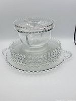 Photo showing a stack of the Candlewick glassware including the serving platter with handles, luncheon plates, and divided serving dishes, all with characteristic beaded edges.