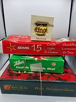 Photo showing the sealed packages stacked: Sears 15 candle lights in clusters, Alderbrook stained glass style ornament box, Zellers Christmas decoration box, and a box of hand decorated glass items with floral design.