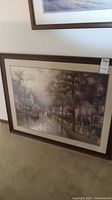 Framed Thomas Kinkade art print showing a rainy village street scene with houses, trees, and a church steeple.