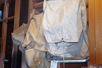Two beige canvas backpacks stacked against a wall, showing the main flap covering the top with a drawstring closure.