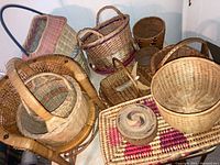 Wide view of multiple wicker baskets of different shapes and sizes, a miniature wicker chair, and woven mats.