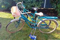 Full view of two vintage bicycles on grass, teal frames, basket on Firestone bike.