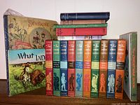 Front view of book lot showing 10 volume New Junior Classics set in colorful spines, vintage children's books including Sunshine and What India Taught the World, and The Christmas Book.