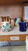 Four ceramic pitchers and tea pots on wooden shelf with handwritten label 'Lot'.