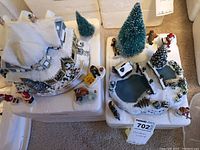 Overhead photo showing village home, pond with bridge, trees, Santa, Mrs. Claus, villagers, and snowman arranged on white packing styrofoam.