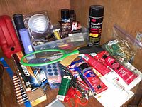 Photo showing assortment of tools including flashlights, glue tubes, batteries, furniture touch-up kit, and other repair items arranged on a wooden surface.
