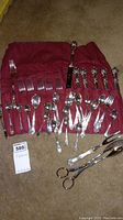 Full view of the flatware set with various forks, spoons, and serving pieces laid out on a red fabric organizer.
