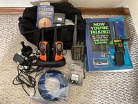 RadioShack and Icom handheld ham radios with accessories laid out on carpet including carrying bag, instruction books, charging dock, antennas, and cables
