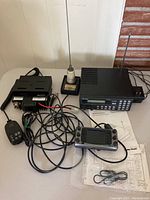 Wide shot of all items: Radio Shack Pro-2030 scanner, Icom IC-2800 receiver, Larson antenna, microphone, cables, and manual on table.