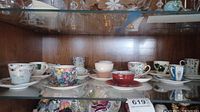 Glass shelf with a variety of vintage teacups and saucers, assorted floral designs and colors