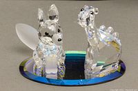 Front view of the baby fox and baby dinosaur Swarovski crystal figurines displayed on the beveled oval mirror base, showing their detailed faceted bodies and black eyes.