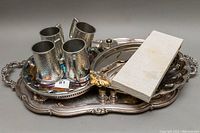 Front view of 4 Birks English pewter hammered beer stein mugs arranged on a ornate oval silver-tone tray with handles, accompanied by a rectangular case (carving set) and additional smaller trays beneath.