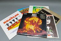 Six classic rock vinyl records displayed with visible cover art highlighting KISS, Beatles, Boston, Beach Boys and Hair soundtrack.