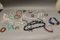 Photo showing assortment of costume necklaces and bangles on a gray background, including faux pearl, wooden bead, turquoise, black and silver bead necklaces plus various bangles.