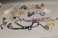 Various costume necklaces and bangles arranged on a surface with a light gray background including pearl and multicolored beads along with two silver-tone bangles.