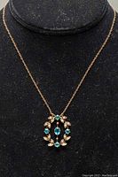 Full view of 16-inch rose gold chain with attached oval wreath pendant displayed on black bust