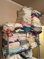 Side view of metal shelving stacked with folded assorted bath towels and bed sheets in assorted colors, mostly pastels and neutrals.