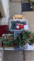 Overall view of multiple storage bins and boxes containing Christmas decorations such as lights, ornaments, and greenery.