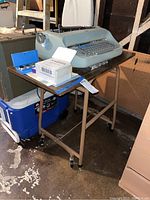 Side view of the IBM electric typewriter resting on a brown metal stand with wheels.