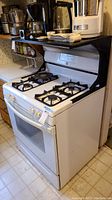 Side view of the white Kenmore gas stove with four burners and attached black shelf