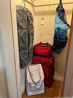 View of all luggage items including the gray garment bag, two red luggage bags stacked, the patterned overnight bag, and the blue hanging bag