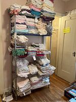 Full view of metal shelving unit fully loaded with stacked linens in a room.