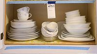 Full view of cabinet shelf showing Mikasa Gabriele cups and saucers stacked on left, Corelle white plates stacked on right, and white bowls with glass bowls in center.