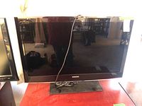 Front view of Samsung 40-inch flat-screen TV showing screen, bezel with Samsung logo, and base stand. Bundled remote is placed on stand base.