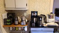 Wide view on kitchen counter showing all appliances together including coffee maker, juicers, food chopper, spice grinder, and water packs.