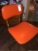 Front view of vintage orange vinyl office chair with wooden frame and caster wheels.