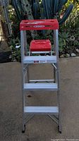 Front view of Werner aluminum step ladder with red plastic tool tray showing three steps and feet caps.