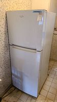 Full view of white Whirlpool refrigerator showing exterior front and side, positioned against floral wallpaper and tiled floor.